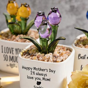 May include: White ceramic pots with glass tulip flowers in yellow, purple, and blue. The pots have text that reads "I LOVE YOU SO MUCH" and "Happy Mother's Day I'll always love you, Mom!" and "Best mom ever".