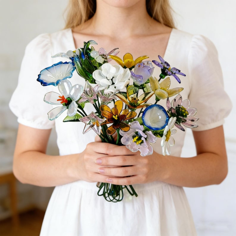 May include: A colorful bouquet of glass flowers in various shapes and colors, including white, blue, yellow, and orange. The flowers are held together with green wire stems, creating a delicate and artistic arrangement.