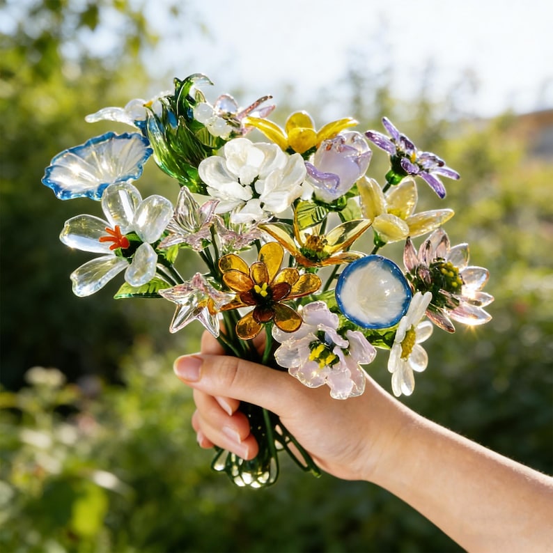 May include: A colorful bouquet of glass flowers in various shapes and colors, including blue, white, yellow, and purple. The flowers are held together with green stems, creating a vibrant and artistic display.