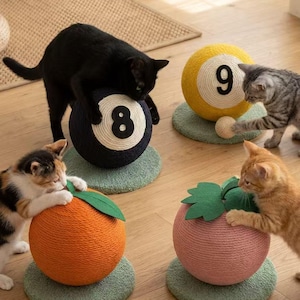 Könnte beinhalten: Verspielte Szene mit Katzen, die mit Kratzbäumen in Form von Billardkugeln und Früchten interagieren. Die Kratzbäume sind orange, rosa, gelb und schwarz, mit Zahlen auf den Billardkugeln. Sie stehen auf grünen runden Matten.