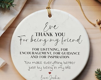 May include: A white ceramic ornament with a gold string for hanging. The ornament has a marble-like texture and features the text "Eve, Thank You For being my friend" and a heartfelt message. A small red heart is included.