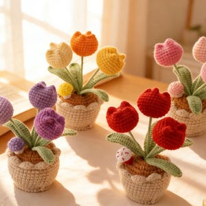 以下が含まれることがあります： 小さな織りポットに入った、手作りのかぎ針編みのチューリップの花のコレクション。 チューリップは、紫、オレンジ、黄色、赤、ピンクなど、さまざまな色があります。 葉は緑色で、ポットはベージュ色です。