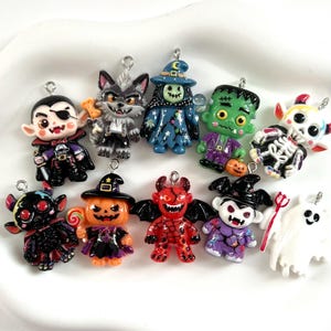 May include: A collection of ten colorful Halloween-themed charms featuring various characters including a vampire, werewolf, witch, Frankenstein's monster, skeleton, devil, pumpkin, and ghost, each with a small metal loop for attachment.