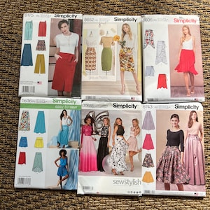 May include: Six Simplicity sewing pattern envelopes featuring various skirt designs, including pencil, wrap, pleated, and A-line styles. Each envelope displays illustrations of finished garments, model photographs, pattern numbers, and instructional text.