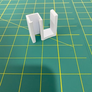 May include: A white plastic 3D printed U-shaped bracket.