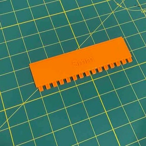 May include: An orange plastic comb with 5mm teeth. The comb is on a green cutting mat.