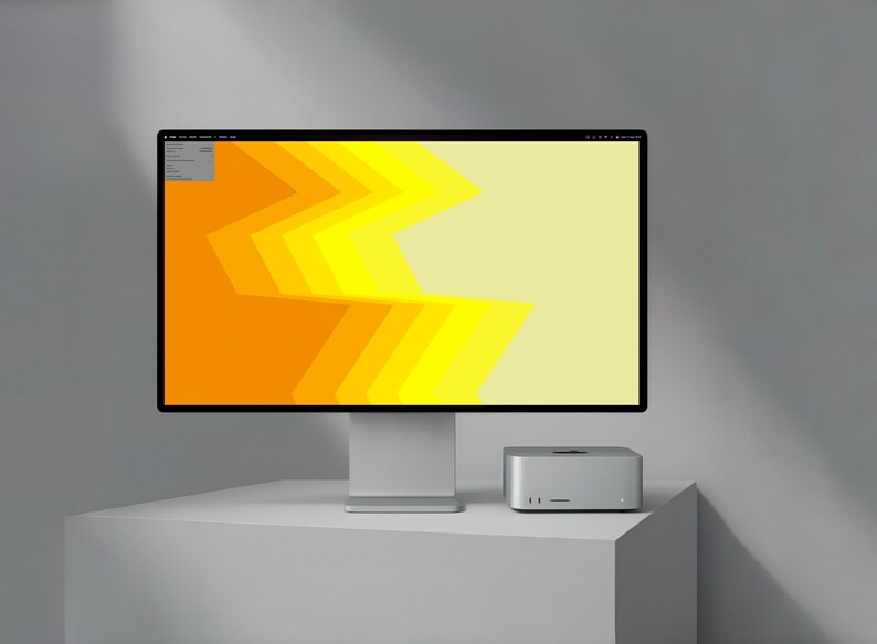 May include: A modern computer setup featuring a large monitor with a vibrant yellow and orange geometric design. A small, silver computer sits beside the monitor on a white surface. The setup is against a gray background.