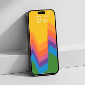 Puede incluir: Un smartphone moderno con un fondo de pantalla abstracto y colorido que presenta un degradado de naranja, amarillo, rosa, morado, azul y verde. La pantalla muestra la fecha y la hora. El teléfono está apoyado contra una superficie blanca.