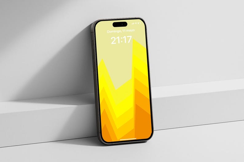 May include: A black smartphone with a yellow and orange geometric design on the screen, leaning against a white surface. The screen displays the date and time. The phone has a sleek, modern design.
