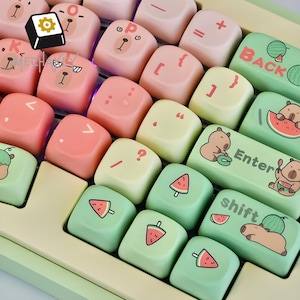 Op de afbeelding: Close-up van een aangepast toetsenbord met pastelkleurige toetsdoppen. De toetsdoppen hebben beer- en watermeloenontwerpen, samen met symbolen en letters. Het toetsenbord heeft een lichtgroen en crèmekleurig kleurenschema.