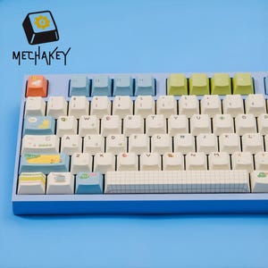 May include: A light blue mechanical keyboard with white keycaps and colorful accent keys. The keyboard has a grid-patterned space bar and the text "MECHAKEY" is visible. The keycaps feature various symbols and designs.