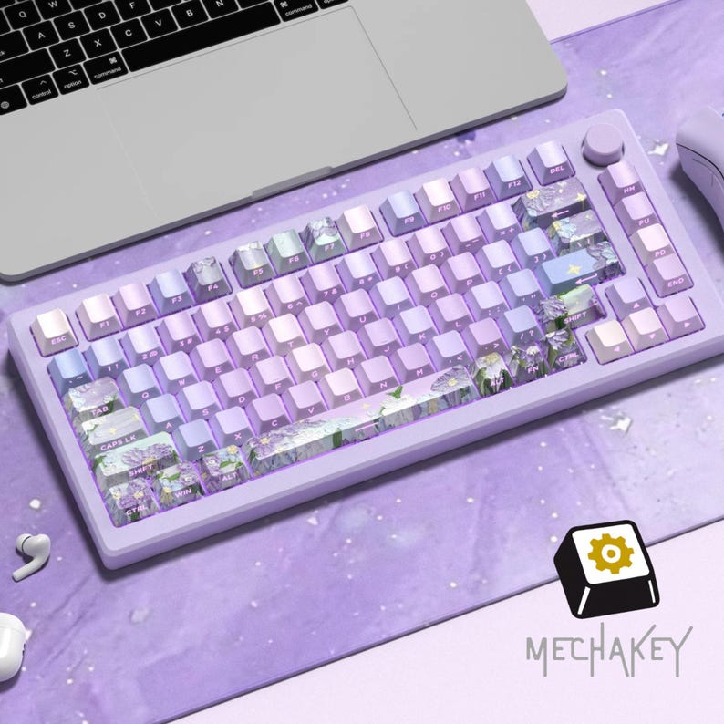May include: A lavender mechanical keyboard with white and purple keycaps. Some keycaps have a floral design. The keyboard is on a purple surface with a laptop and mouse visible. The brand name "MECHAKEY" is displayed.
