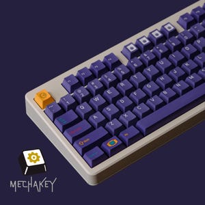 May include: A mechanical keyboard with purple keycaps and a beige frame. The keys are arranged in a standard QWERTY layout, with a few keys in orange and blue. The keyboard has the text "MECHAKEY" and a logo in the bottom left corner.
