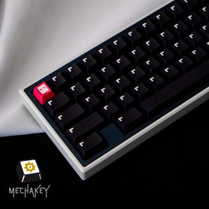 May include: A black and white mechanical keyboard with a white frame and a dark blue accent. The keyboard has black keys with white lettering and a single pink key with a white face. The logo "MECHAKEY" is in the bottom left corner.
