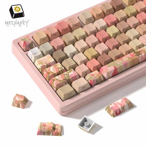 May include: A pink mechanical keyboard with gradient keycaps in shades of beige, pink, and green. Some keycaps have a floral pattern. The keyboard has the text "MECHAKEY" on the top left.