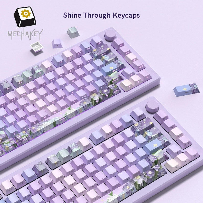 May include: Two light purple mechanical keyboards with gradient keycaps. The keycaps feature floral and star designs, with the text "Shine Through Keycaps" above. The brand name "MECHAKEY" is visible in the upper left corner.