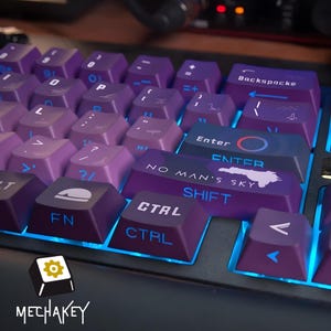 May include: A close-up of a mechanical keyboard with purple keycaps and blue backlighting. The keycaps have white and blue lettering and symbols. Some keys have the text "NO MAN'S SKY" and "CTRL". The keyboard has the logo "MECHAKEY".