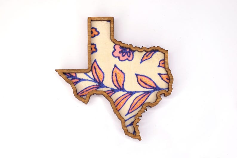 May include: Wooden Texas-shaped decorative item with a floral design. The interior features a cream-colored background with pink flowers and orange and blue leaves. The border is a natural wood color.