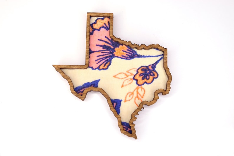 May include: Wooden Texas-shaped decorative item with a floral design. The interior features a cream-colored background with pink, blue, and orange flowers. The wooden frame has a natural wood grain finish.