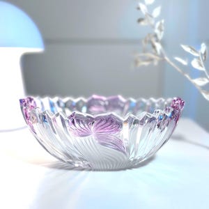 May include: A clear glass bowl with a scalloped rim and a floral design in shades of purple. The bowl has a textured, etched pattern and is likely used for decorative purposes.