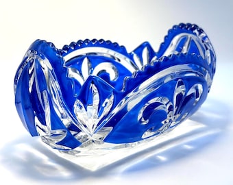 May include: A decorative, blue glass bowl with intricate cut patterns. The bowl features a vibrant blue color and a clear, rectangular base. The rim has a scalloped edge, and the design includes floral and swirling motifs. The bowl is likely used for decorative purposes.