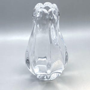 Könnte beinhalten: Eine klare Glasvase in tulpenartiger Form. Die Vase hat einen breiten Boden, der sich nach oben verjüngt, mit einer geriffelten Oberseite. Das Glas ist glatt und transparent und reflektiert das Licht. Die Vase ist für Blumen oder andere dekorative Gegenstände konzipiert.