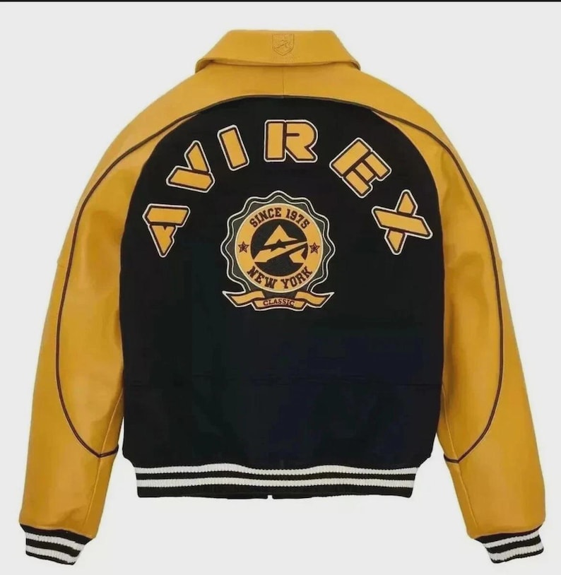K&ouml;nnte beinhalten: Schwarz-gelbe Collegejacke mit dem Wort "AVIREX" auf dem R&uuml;cken. Die Jacke hat ein klassisches Design mit schwarzem K&ouml;rper, gelben &Auml;rmeln und einem wei&szlig;-schwarz gestreiften Saum. Auf der R&uuml;ckseite befindet sich ein Emblem "Since 1975 New York Classic".