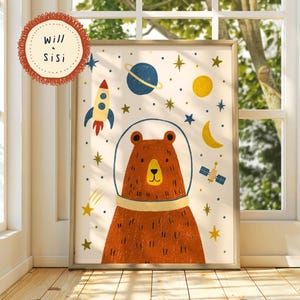 May include: A framed wall art print featuring a brown bear wearing a space helmet, surrounded by a rocket, a blue planet with rings, a yellow sun, a crescent moon, a satellite, and various stars on a cream background with the text Will & Sisi.
