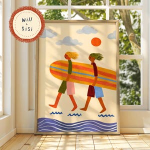 May include: A framed art print featuring two figures carrying a large orange, yellow, and blue surfboard across a beach. The scene includes a bright orange sun, light blue clouds, and stylised blue waves. The text Will & Sisi appears in a circle.