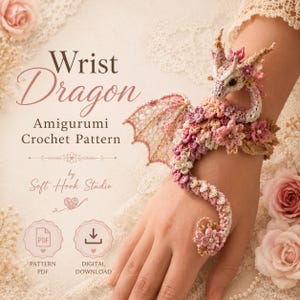 May include: A crochet wrist dragon amigurumi pattern by Soft Hook Studio. The image features a delicate, light-colored dragon adorned with pink and cream floral details, wrapped around a wrist. Text includes Wrist Dragon Amigurumi Crochet Pattern.