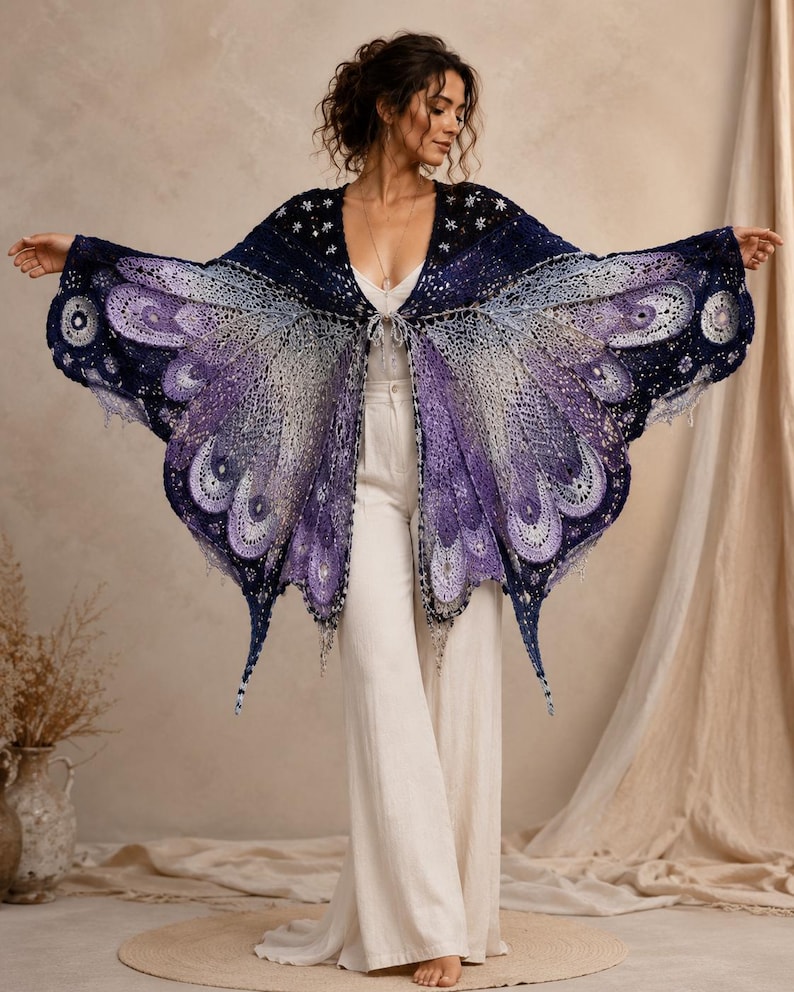 May include: A crochet shawl featuring a butterfly wing pattern in shades of deep navy, violet, and light lavender. The garment has an open front with a tie closure, intricate lace-like stitching, and scalloped edges that mimic the shape of wings.