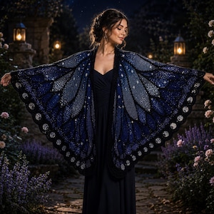 May include: A dark blue and black shawl designed to resemble butterfly wings, featuring intricate patterns of stars and moon phases. The garment is worn over a simple dark navy dress, with the shawl extending outward to display its wing-like shape.