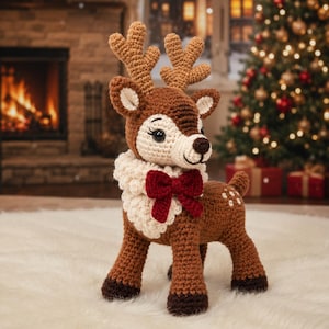 May include: A crocheted reindeer figurine featuring a brown body with white spots, a cream-colored textured neck ruff, and a dark red bow. The reindeer has large antlers, dark brown hooves, and a cream-colored face with black eyes.