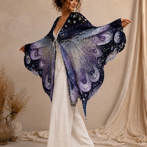 May include: An oversized crochet shawl featuring a butterfly wing pattern in shades of deep navy, violet, and light lavender. The intricate openwork design includes circular motifs and star-like accents. The text Oversized Butterfly Fit is visible.