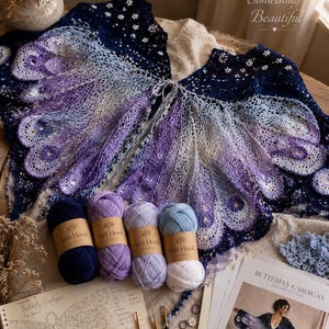 May include: A crochet butterfly cardigan featuring a gradient of blue, purple, and white yarn, displayed with four skeins of yarn, crochet hooks, stitch markers, and a printed pattern titled Butterfly Cardigan with the text Create Something Beautiful.