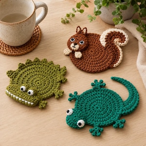May include: Three crocheted animal coasters featuring a brown squirrel with a cream tail, a green crocodile with white teeth, and a teal lizard. Each coaster has round black and white eyes and is crafted with textured yarn in distinct shapes.