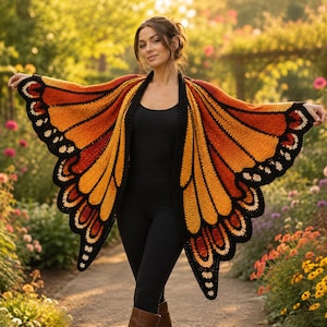 May include: A crochet shawl designed to resemble monarch butterfly wings, featuring vibrant orange, yellow, and deep red segments outlined in black with white accents along the scalloped edges, worn over a simple black top and black leggings.