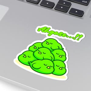 Puede incluir: Una pegatina con un grupo de personajes verdes de dibujos animados con los ojos cerrados, sobre un fondo blanco con un borde amarillo. La pegatina tiene el texto "Ahgase...!!" en verde, con una fuente estilizada.