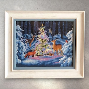 Puede incluir: Obra de arte de punto de cruz de una escena de bosque invernal, enmarcada en un marco de madera blanco. La escena representa un bosque nevado con un árbol de Navidad decorado, ciervos, un zorro y otros animales salvajes.