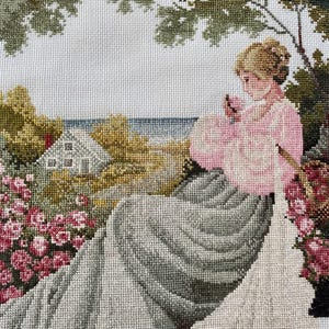 May include: A detailed needlepoint tapestry depicting a woman in a pink dress seated in a garden. The scene includes a house, flowers, and trees, with a coastal view in the background. The artwork is rendered in a cross-stitch style.