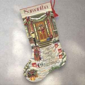 Könnte beinhalten: Bestickter Weihnachtsstrumpf mit dem Namen "Samantha" oben. Das Design zeigt ein Haus mit einem Kranz an der Tür, Schnee und dem Text "All hearts come home for Christmas."