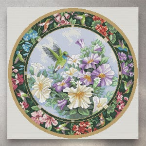 May include: A cross-stitch design depicting a central floral arrangement of white and purple petunias, with a hummingbird in flight. The design is framed by a green border with hummingbirds and flowers, set against a light blue backdrop.