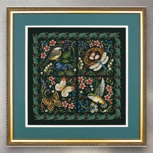 May include: Framed cross-stitch artwork depicting a nature scene. The design includes a bird, butterfly, hummingbird, dragonfly, and a nest with eggs, surrounded by flowers and foliage. The artwork is framed in gold with a green mount.
