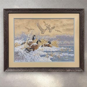 Könnte beinhalten: Gerahmtes Kunstwerk, das eine Winterszene mit Gänsen zeigt. Das Kunstwerk zeigt mehrere Gänse, die im Schnee in der Nähe eines Gewässers ruhen, mit anderen Gänsen, die im Hintergrund fliegen. Der Rahmen ist aus dunklem, verwittertem Holz.