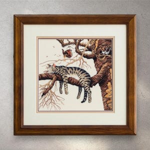 以下が含まれることがあります： 額縁に入ったクロスステッチのアートワークは、木の枝で眠っているトラ猫を描いています。猫はグレーと黒の縞模様です。木は茶色で、小さな枝と赤い鳥小屋があります。アートワークは茶色の木製フレームに入っています。