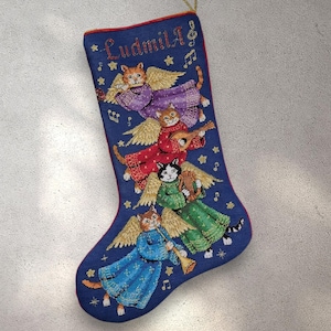 Puede incluir: Calcetín navideño azul con gatos ángeles bordados tocando instrumentos musicales. El calcetín tiene un ribete rojo y el nombre "Ludmila" bordado en la parte superior. Cuerda dorada para colgar.