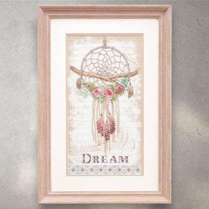 May include: Framed artwork with a dreamcatcher design. The dreamcatcher is decorated with pink roses, feathers, and macrame. The word "DREAM" is displayed in a decorative font at the bottom. The artwork is framed in a light brown wooden frame.