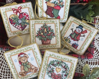 May include: A collection of six square Christmas ornaments with embroidered designs. Each ornament features a different holiday theme, including a snowman, teddy bear, and Christmas tree. The ornaments have gold trim and hanging loops.