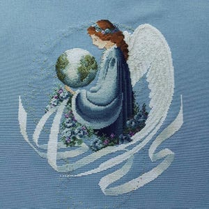 May include: Cross-stitch design of an angel in a blue gown, holding a globe. The angel has white wings and red hair, surrounded by white ribbons and blue flowers. The background is a light blue fabric.