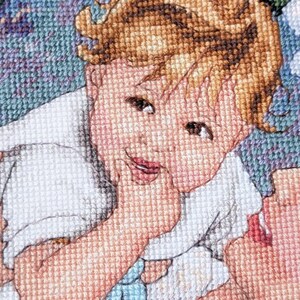 May include: A cross-stitch portrait of a smiling child with light brown hair and rosy cheeks. The child is wearing a white garment and is touching their face. The background is a mix of blue, green, and purple.